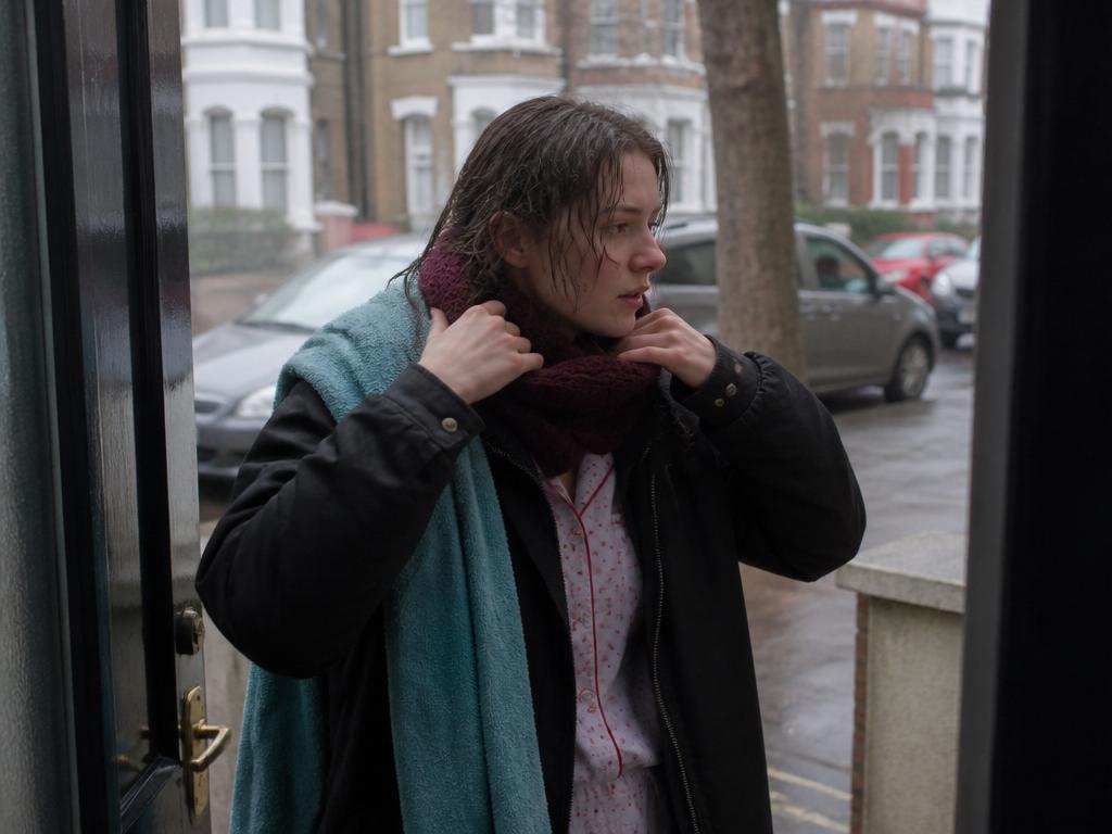 A young woman with wet hair stepping outside into a cold grey morning, pulling up a scarf