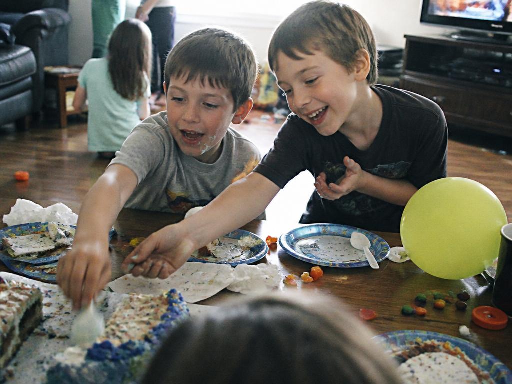 Children reaching for cake and candy at a messy living-room birthday party